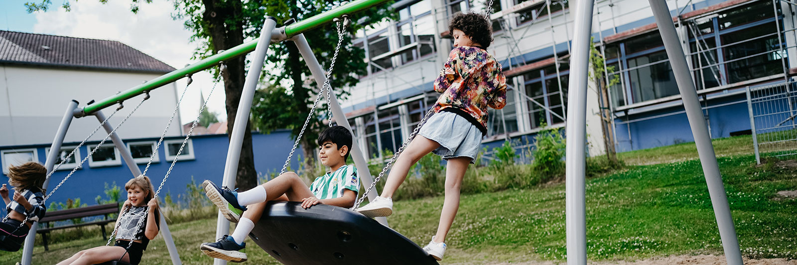 A large swing set frame, with multiple different swing seats, children swing on them in different ways.